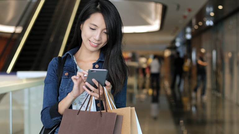 shopping-woman-using-cellphone-and-holding-shoppin-UPBBMA8